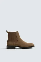 Bota estilo Chelsea de piel con acabado serraje color marrón claro, con elásticos laterales para facilitar el calce. Tiene horma redonda y suela con ligero tacón.