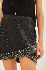 Falda corta de tiro medio con bordado de lentejuelas y piedras en el ruedo. Presenta un diseño cruzado con cierre en la espalda y forrería a tono.