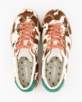 Championes de edición limitada con estampado de vaca en tonos marrón y blanco, cordones naranjas, talón verde y suela de goma color miel.