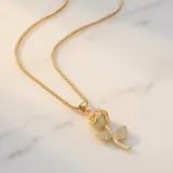 Cadena de acero con baño de oro y dije de bronce con forma de rosa, decorado con circonias incrustadas.