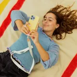 Correa universal para teléfono color crema con logo de la marca estampado en la cinta y parche de cuero sintético color beige.