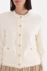 Saco de punto estilo tweed en color natural, con cuello redondo, cierre frontal de botones dorados y detalles de flecos en los bordes, puños y bolsillos frontales.