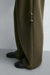 Pantalón de corte wide fit confeccionado en tejido técnico compacto con efecto neopreno. Presenta cintura elástica con cordón ajustable, pliegues frontales, bolsillos laterales y detalle de pliegues en las rodillas con aplicaciones metálicas.