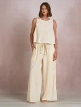 Pantalón palazzo de tiro alto marca Elan, en color beige, confeccionado en mezcla de algodón, viscosa y lino. Presenta cintura delantera plana con parte trasera elastizada, bolsillos laterales funcionales y corte de pierna ancha. Incluye un cinturón trenzado al tono con terminación en borlas y flecos.
