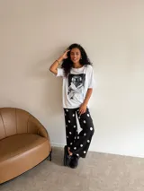 Conjunto compuesto por un remerón blanco de algodón con estampa frontal de un oso con auriculares y taza de café, y un pantalón negro de corte recto con estampado de lunares blancos.