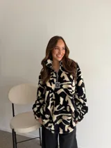 Buzo de peluche con estampado animal print en blanco y negro, cuello alto y cierre frontal con tirador personalizado.