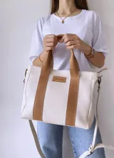 Bolso tipo tote de lona color crudo con detalles en cuero color marrón. Tiene doble asa corta de mano y correa larga de hombro.