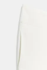 Pantalón negro de tiro alto, con pliegues en el delantero y bolsillos laterales ocultos. Cierre frontal con cremallera y ganchos metálicos.