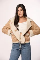 Campera tipo gamulán de gamuza color tostado con interior y solapas de corderito sintético color crema. Presenta cierre frontal con botones, bolsillos cuadrados delanteros y detalles de costuras visibles.