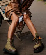 Botas de caña baja con base de terciopelo y paños de tweed a cuadros en tonos marrones, beige y verde. Presentan detalles en cuero marrón y cordones marrones.