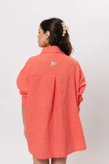 Camisa larga amplia color coral con patrón a cuadros, cuello camisero, cierre frontal con botones y grandes bolsillos en el pecho.