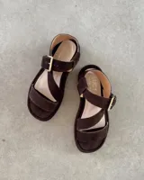 Sandalias de gamuza color marrón con diseño de tiras cruzadas, puntera abierta y cierre con hebilla metálica dorada en el tobillo.