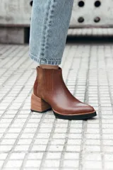 Bota corta de cuero color marrón, con diseño de texturas combinadas en los laterales y elástico. Presenta un taco medio de madera y suela de goma negra.