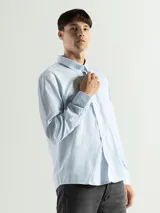 Camisa celeste y blanca a cuadros con cuello abotonado, manga larga y bolsillo en el pecho.