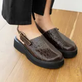 Sueco de cuero vacuno color marrón con estampado de cocodrilo, suela de goma negra y hebilla metálica plateada.