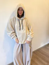 Buzo tipo hoodie de tela de peluche color beige, con capucha y cordones ajustables. Presenta un diseño holgado con mangas largas y puños elásticos.