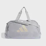Bolso deportivo Adidas de color gris claro con logo estampado en tono beige. Cuenta con compartimento principal con cierre, bolsillo frontal con cremallera, correas de mano y correa de hombro ajustable con hombrera acolchada.