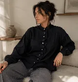 Camisa negra de calce relajado con cuello mao, cierre frontal de botones y detalle de volado vertical en el frente. Presenta mangas largas con puños abotonados.