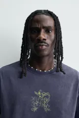 Camiseta de corte relajado con cuello redondo y manga corta. Presenta un acabado con efecto lavado que le otorga una apariencia única y desgastada. Incluye estampados a contraste en la parte frontal.