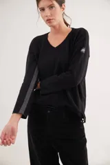 Buzo de escote en V y manga larga, confeccionado en lana lambswool. Presenta un diseño básico con detalle de raya en contratono en una de las mangas, puños y ruedo en color contrastante, y pin metálico de la marca aplicado en la manga.
