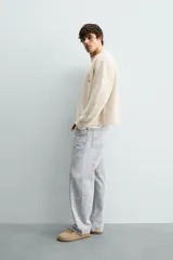 Cárdigan de punto color beige con cuello en pico, manga larga y cierre frontal de botones. Presenta un pequeño bordado a contraste en el pecho y acabados en rib en puños y bajo.