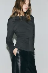 Top de manga larga confeccionado en punto de algodón, con cuello redondo, hombros caídos y detalle de frunces laterales que generan un bajo acampanado.