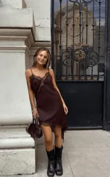 Vestido midi slip dress color marrón, de satén con tirantes finos y detalles de encaje en el escote y el dobladillo asimétrico.