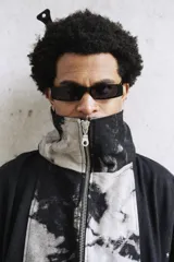 Campera unisex de cuello alto con cierre frontal completo. Presenta un diseño de paneles con efecto de lavado ácido en tonos negro y gris, corte relajado y bolsillos laterales.