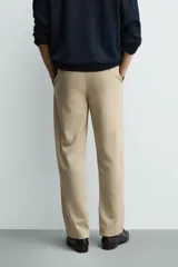 Pantalón de corte recto confeccionado en tejido elástico, con cintura elástica, pliegues frontales, bolsillos laterales y bolsillos traseros de vivo con botón.