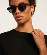 Suéter negro de punto con cuello redondo y mangas largas. Tiene un dobladillo superpuesto de camisa blanca.