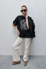 Remera negra de silueta amplia y calce relajado, con cuello redondo, mangas cortas con hombros caídos y estampa botánica en líneas blancas en el frente.