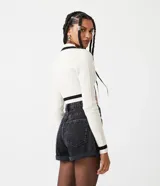 Suéter cropped de punto texturizado color crema, con escote en V y detalles a contraste en negro en mangas, cuello y busto.