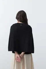 Saco tipo capa de punto color negro, con silueta fluida, corte amplio y cierre frontal con dos botones dorados.