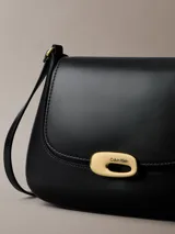 Cartera mediana con solapa Calvin Klein de color negro, confeccionada en poliuretano. Presenta diseño estructurado con cierre de broche a presión metálico dorado y correa ajustable.