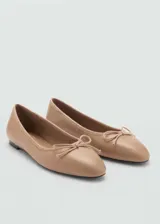 Zapato tipo ballerina de cuero caprino color beige, con punta redondeada y lazo decorativo en la parte frontal.