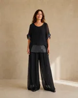 Blusa negra holgada de manga corta translúcida, con cuello redondo y detalles de lentejuelas en el bajo y en las vueltas de las mangas.