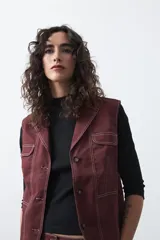 Chaleco de estilo utilitario color bordó con pespuntes blancos a contratono. Presenta solapas, cierre frontal con botones, bolsillos delanteros y un diseño estructurado.