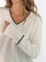 Sweater de punto azul marino con cuello en V, mangas largas con puños acanalados y detalle de línea en color marrón en el cuello y puños. Presenta un pequeño aplique decorativo en la parte inferior.