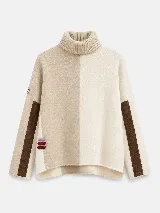 Polera de tejido lambswool con diseño bicolor en tonos neutros. Presenta cuello alto tejido, mangas largas con franjas laterales en color marrón y detalle de bordado artesanal con tres pequeñas líneas horizontales en colores vibrantes.