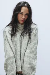 Jersey de punto de corte holgado en color gris jaspeado, con escote en pico y bufanda integrada del mismo tejido. Presenta mangas largas con puños ajustados.