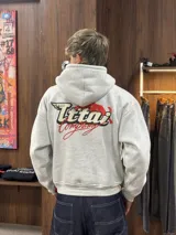 Buzo con capucha gris jaspeado, de corte holgado, con estampado gráfico en la espalda que incluye el texto 'Ittai Company' y una figura de un animal en color rojo.