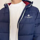 Campera tipo puffer color bordó con capucha, cierre frontal blanco y puños de tejido elástico. Presenta el logo de la marca bordado en el pecho.