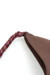 Cartera tipo hobo de gamuza color marrón, con costura central vertical y correa de cuerda trenzada en tonos borró y gris con nudos decorativos en los extremos.