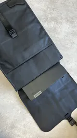 Mochila negra de cuero sintético con solapa superior y cierre con hebilla.