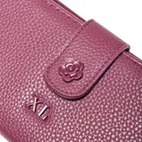 Billetera XL de cuero sintético con textura granulada, color lila. Cuenta con cierre principal, solapa con broche a presión decorada con una flor en relieve y logo de la marca en el frente.