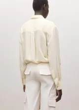 Camisa de seda 100% color marfil, de corte recto, con cuello camisero clásico y cierre frontal de botones ocultos.