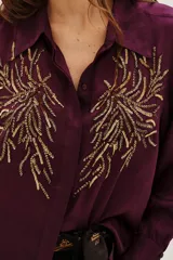 Camisa de viscosa color violeta con cuello clásico, manga larga y cierre frontal con botones. Presenta un diseño bordado con lentejuelas doradas en ambos lados del pecho.