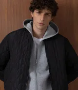 Campera masculina de corte regular, confeccionada en poliéster con acabado capitoneado texturizado en rombos. Presenta cierre frontal con cremallera, cuello redondo y puños con terminación en rib.