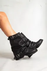 Bota de cuero negro con caña media arrugada, dos correas con hebillas plateadas y taco bajo.