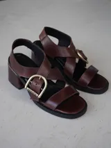 Sandalias de cuero color camel con tiras anchas, taco medio y hebilla metálica en forma de estribo en el lateral.